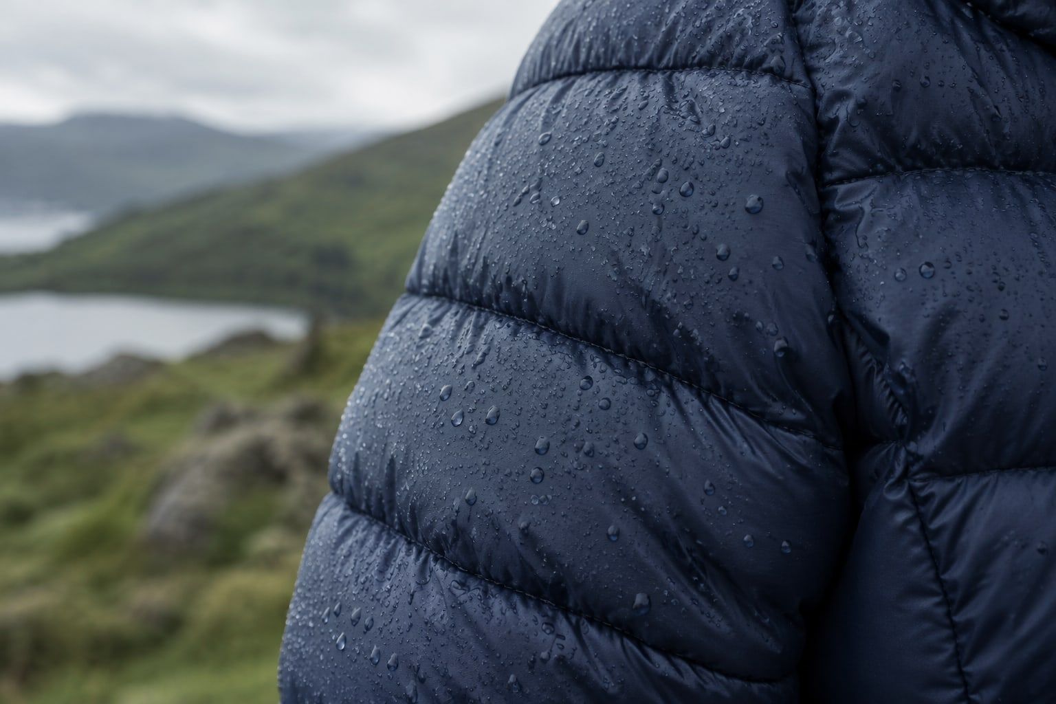 Close-up of a quilted navy puffer jacket with light rain on its baffles.
